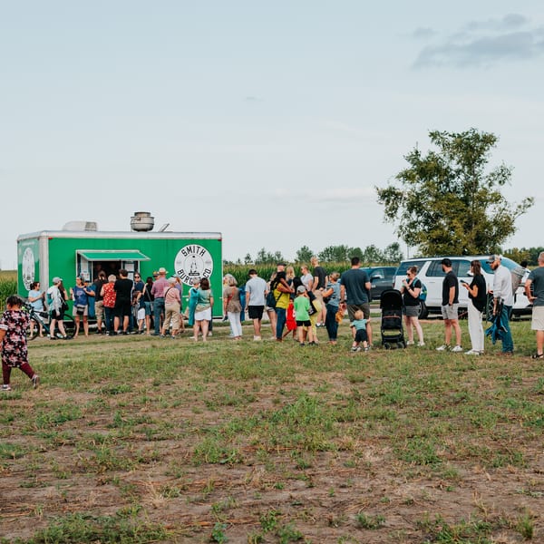 People line up at a green Smith Burger Co. food truck in a grassy field.