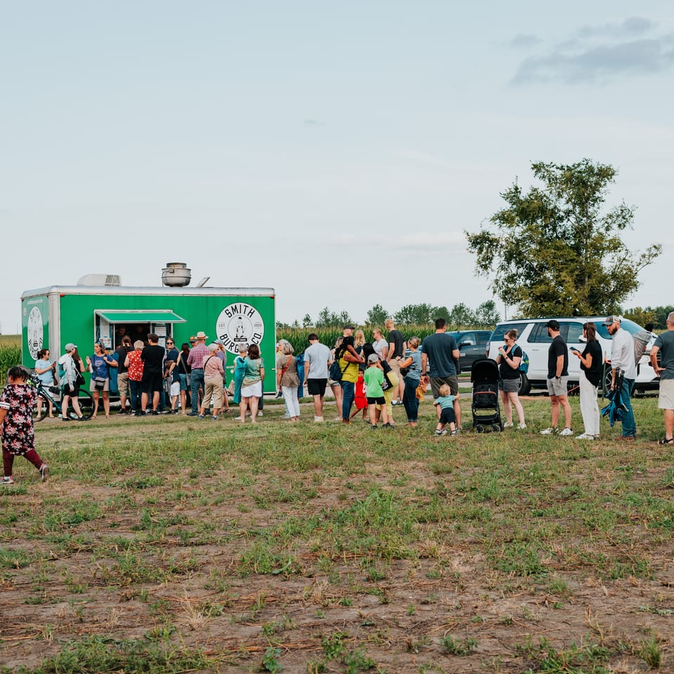 People line up at a green Smith Burger Co. food truck in a grassy field.