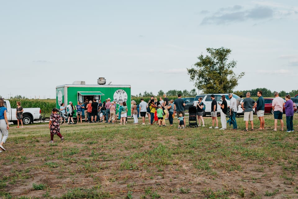 People line up at a green Smith Burger Co. food truck in a grassy field.