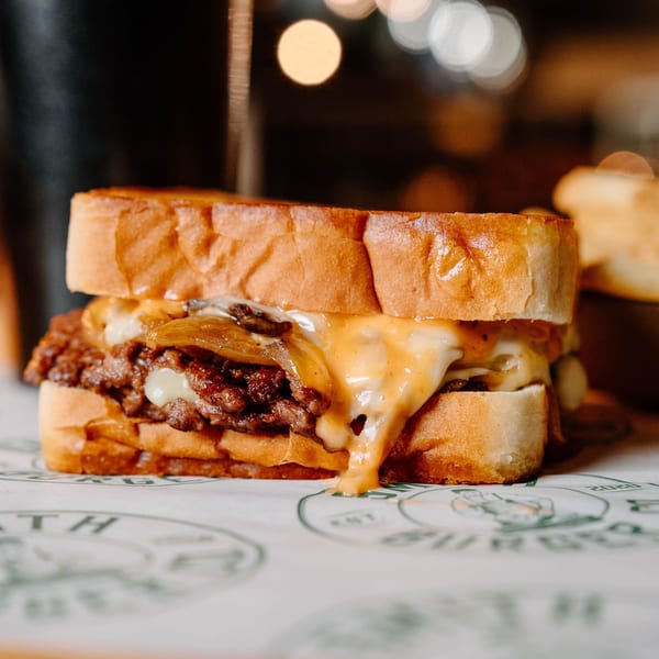 Cheesy steak sandwich with caramelized onions on toasted bread, with fries and dipping sauce in the background.