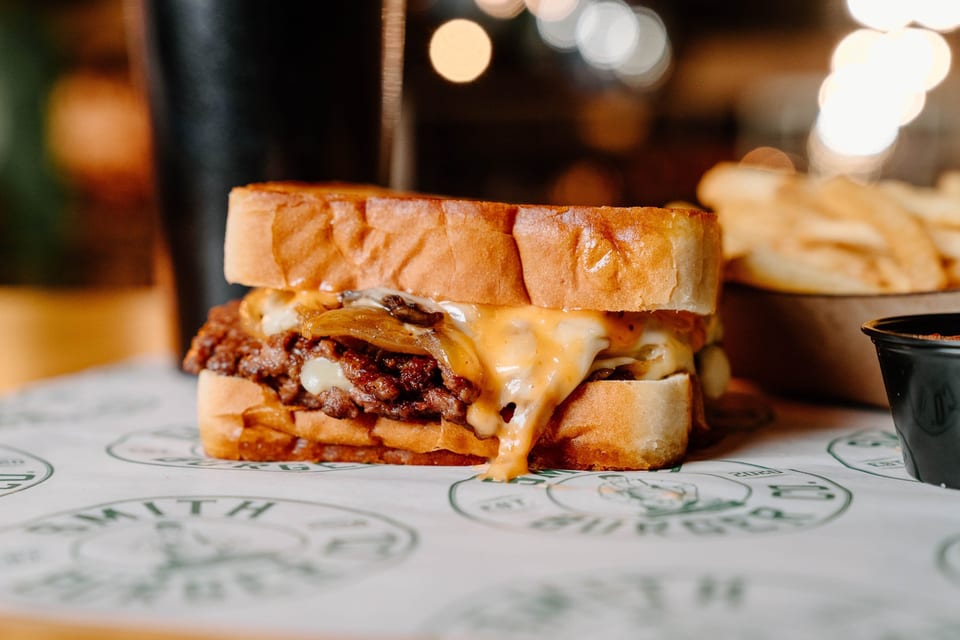 Cheesy steak sandwich with caramelized onions on toasted bread, with fries and dipping sauce in the background.